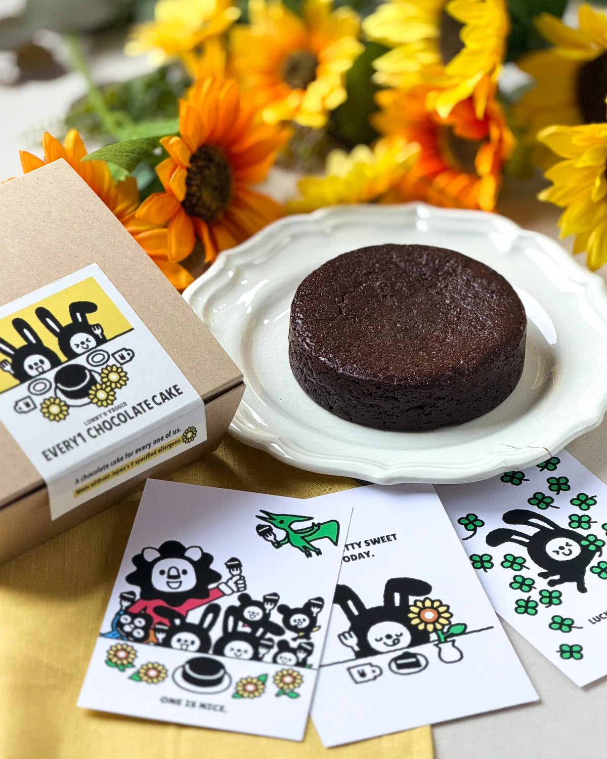 ひまわりとパッケージ、キャラクターカードに囲まれたEvery1 Chocolate Cake